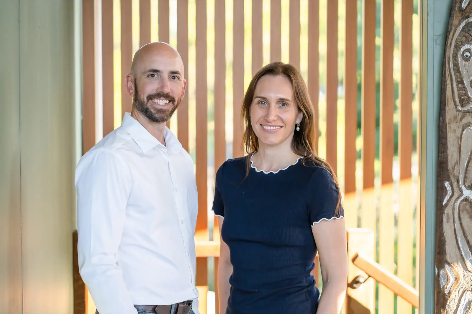Two Grove Support Services support workers standing together by a warm timber screen in natural light