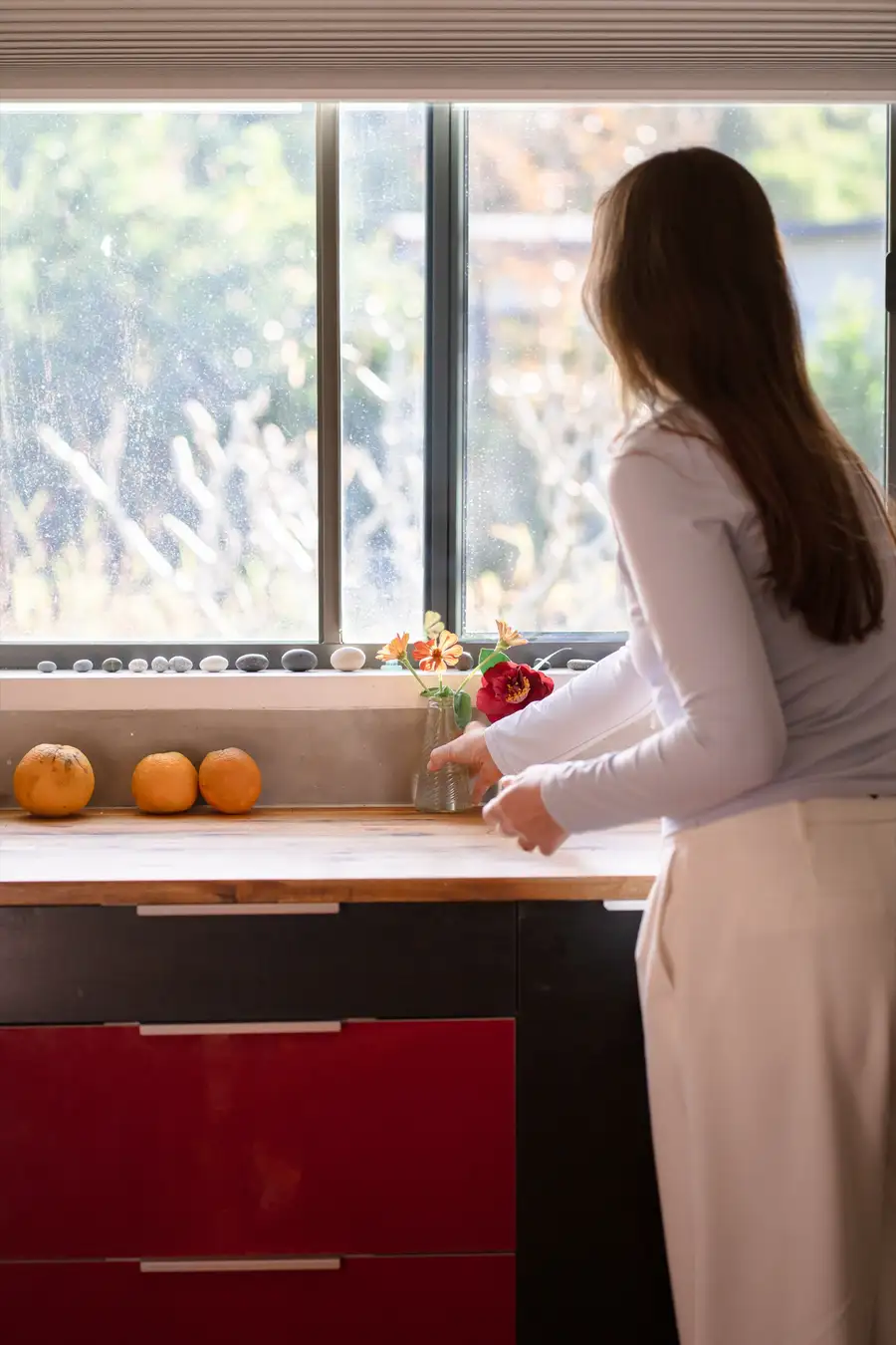 A support worker arranging fresh flowers by a sunlit window in a warm, homely location kitchen