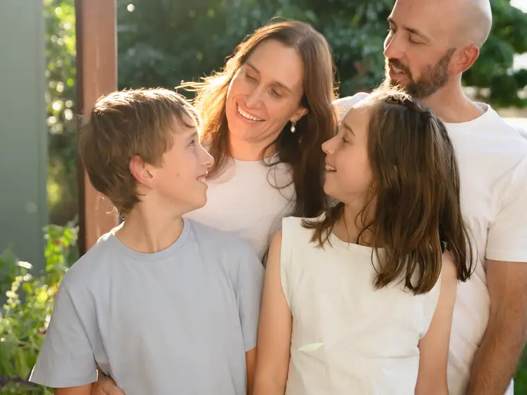 A family of four standing close together outdoors in warm afternoon light