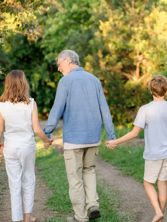 A man walking a grassy trail hand-in-hand with two children