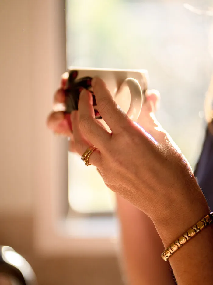 Hands holding a coffee mug by a sunlit window