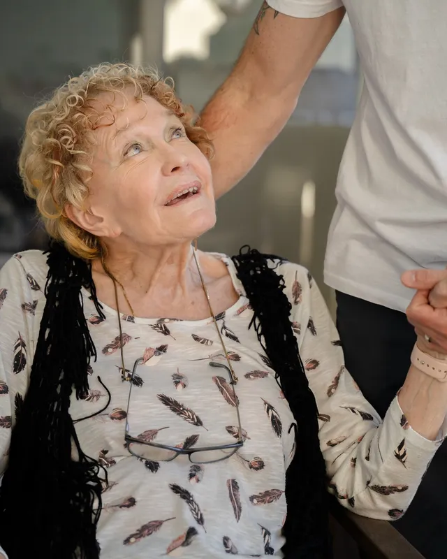 A support worker holding the hand of an older woman indoors